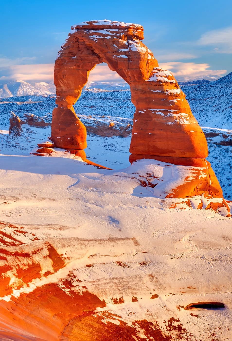 Snow-covered Delicate Arch glowing in warm light, Arches National Park.